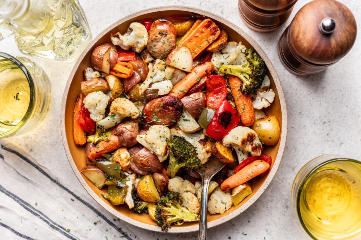A plate of sheet pan sausage and veggies next to salt and pepper mills.