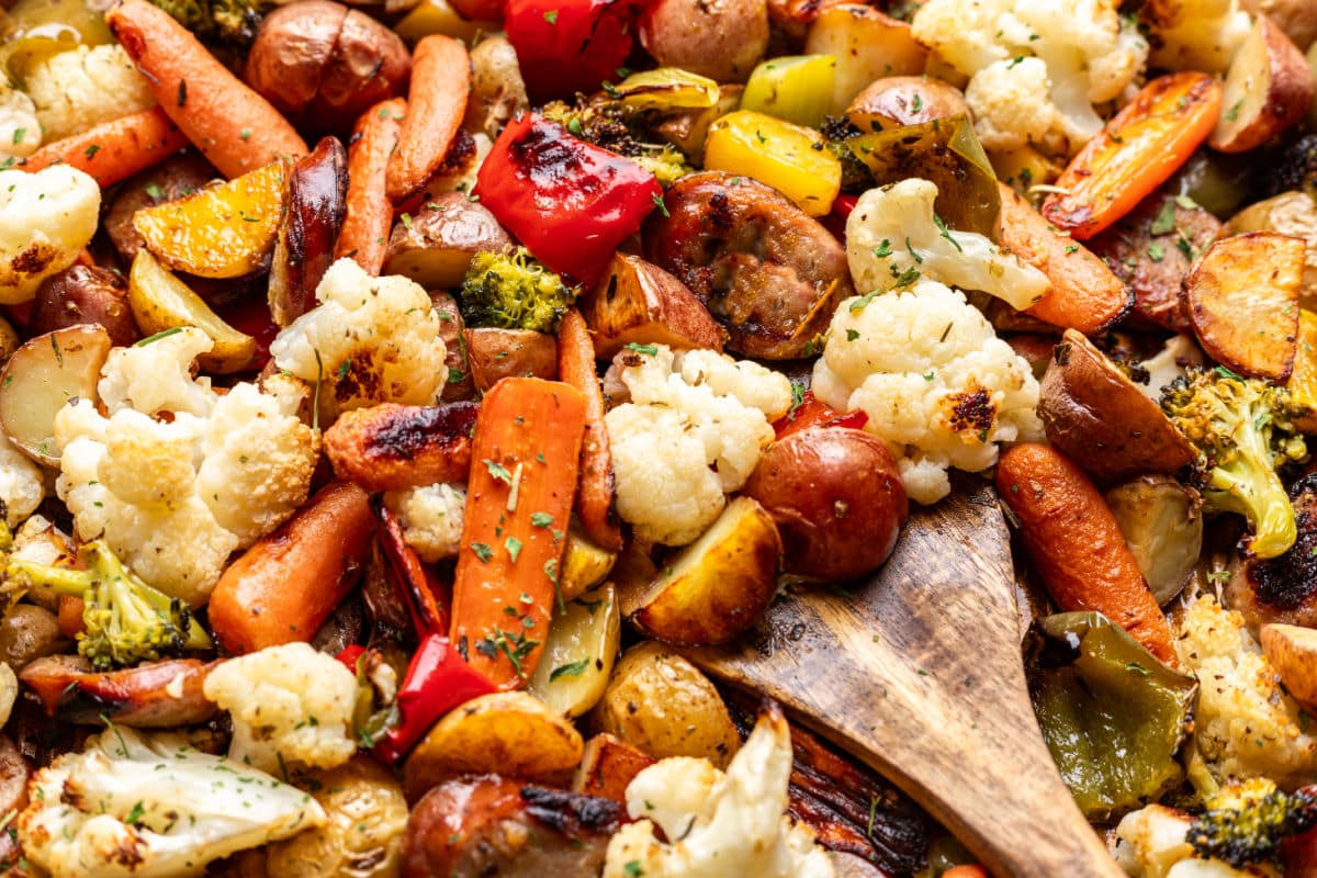 A wooden spoon holding a scoop of sausage and veggies in the pan.