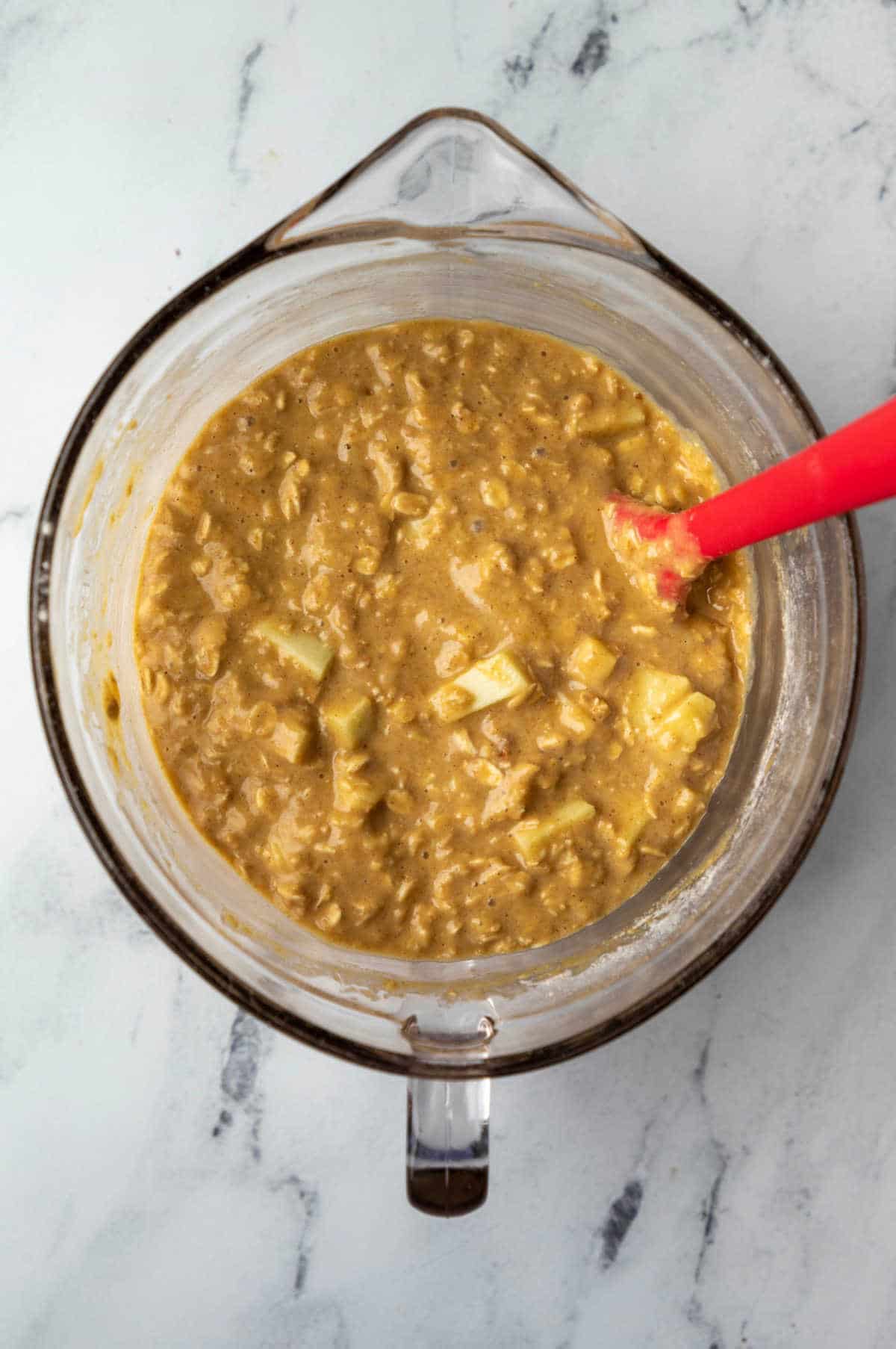 Apple cinnamon oatmeal muffin batter in a glass mixing bowl. 