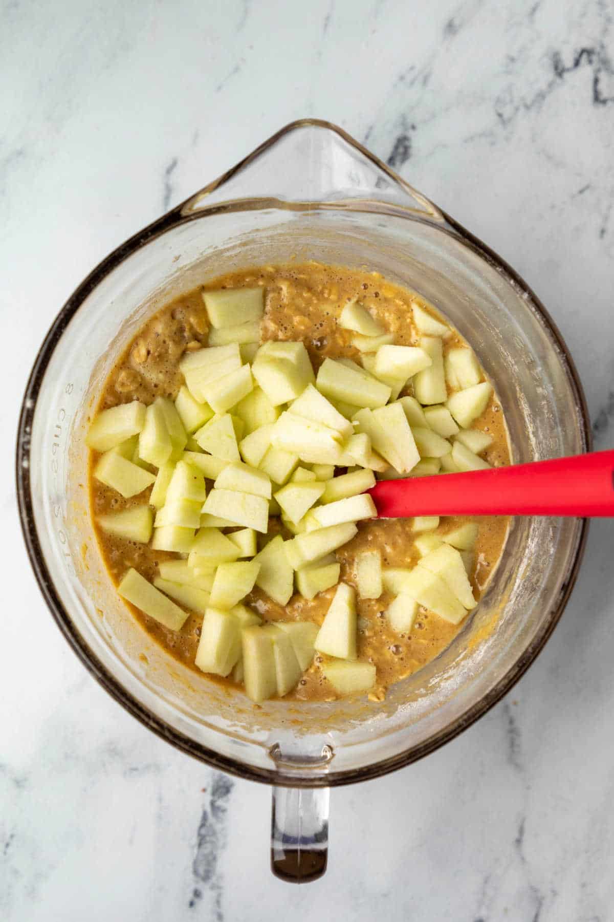 Glass mixing bowl with diced apple on batter. 