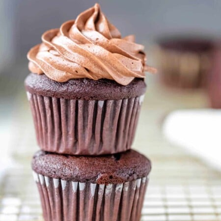 A frosted cupcake sitting on an unfrosted chocolate cupcake.