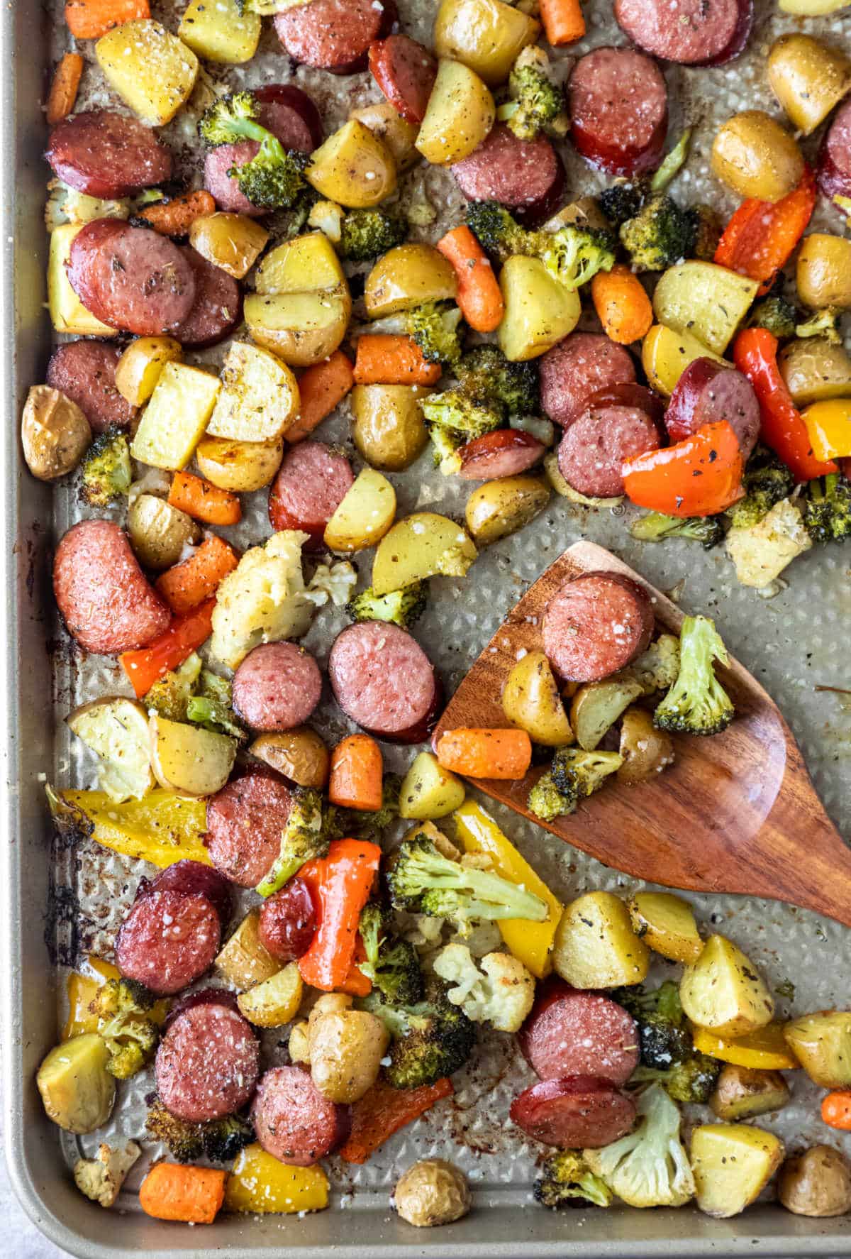 Wooden spoon with roast sausage and vegetables on it.