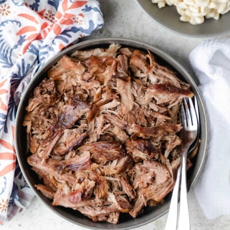 Dish of kalua pork next to a bowl of macaroni salad.