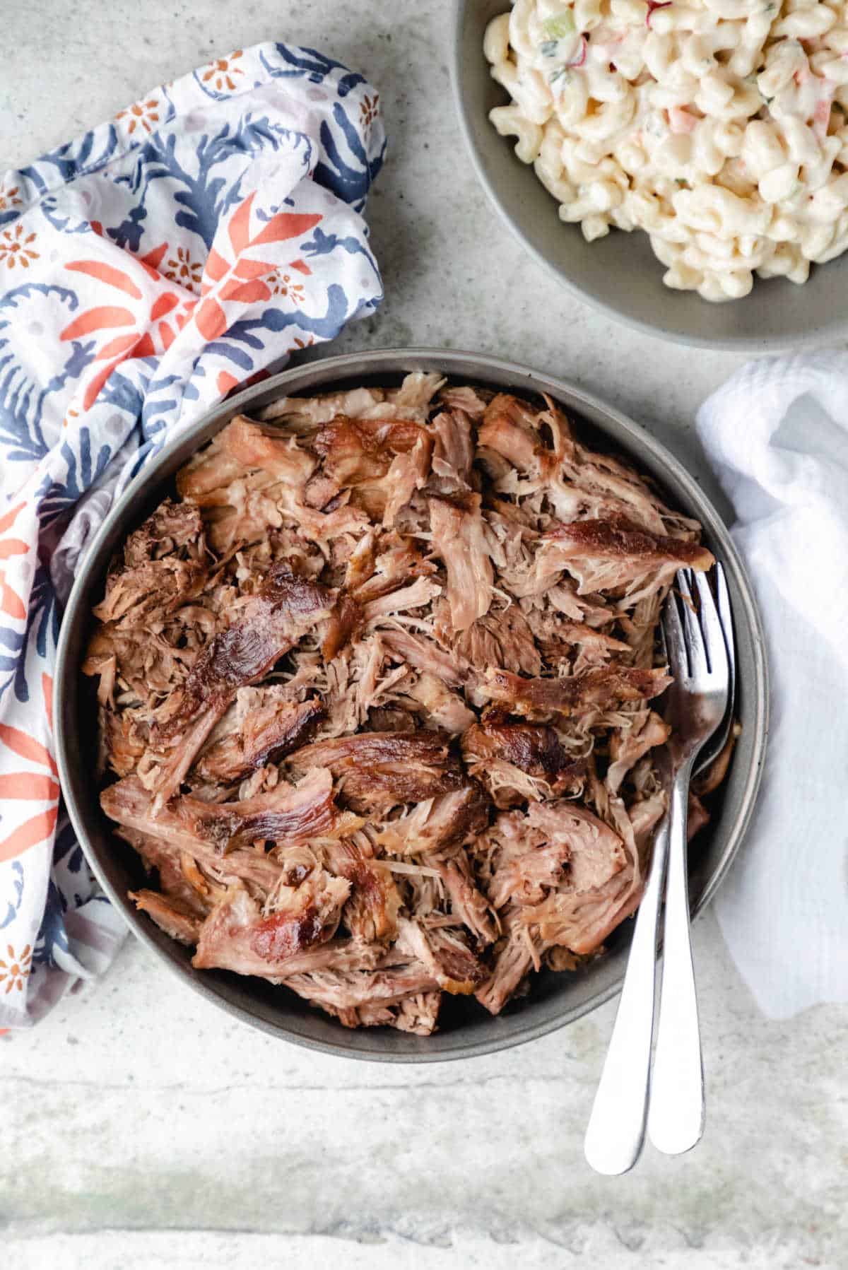 Dish of kalua pork next to a bowl of macaroni salad.