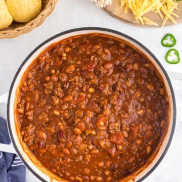 Pot of chili in a Dutch oven next to toppings and cornbread muffins.