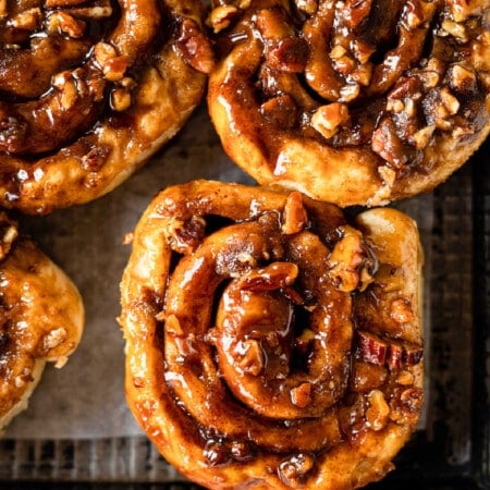 Homemade caramel rolls on a dark metal baking sheet.