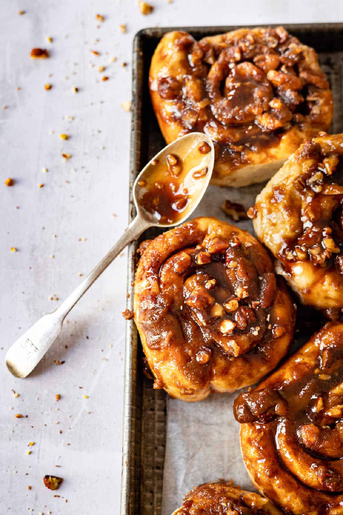 A spoon with caramel sauce next to caramel rolls. 