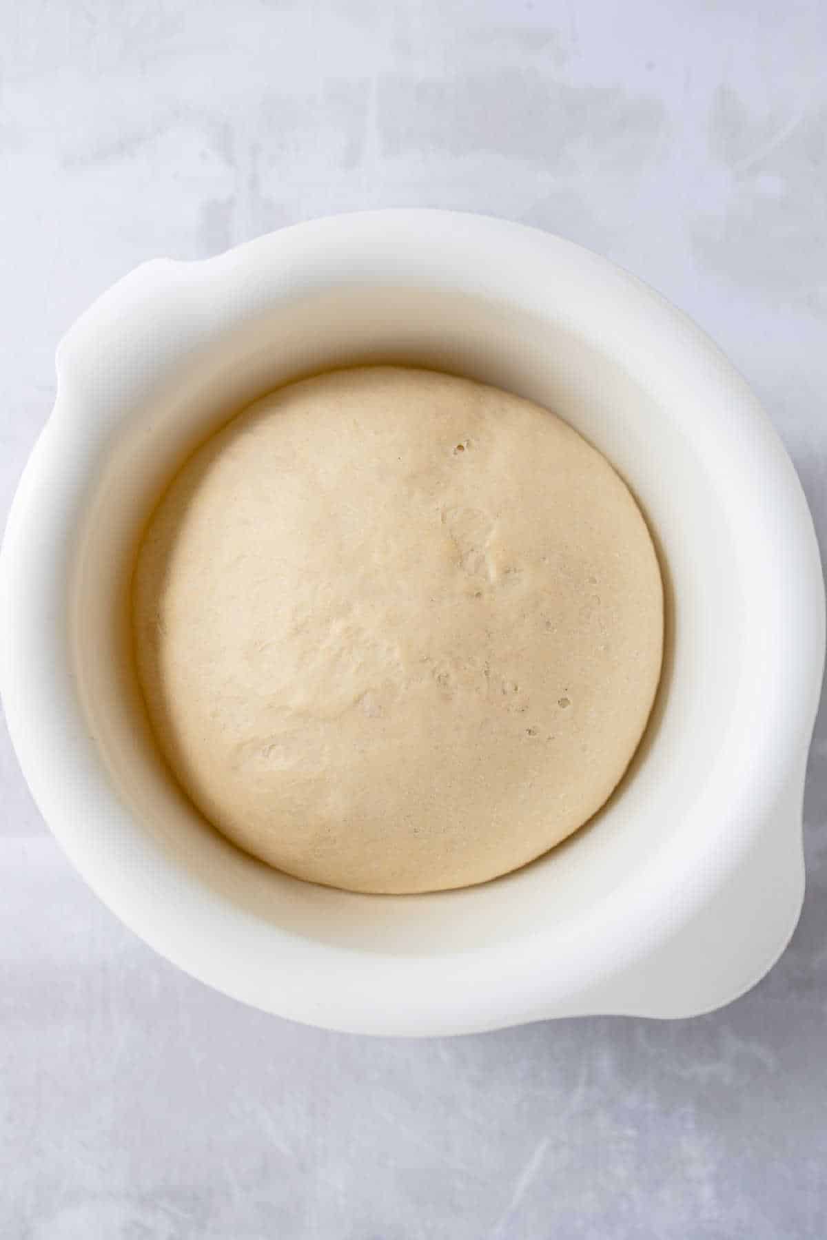 Risen dough in a white mixing bowl. 