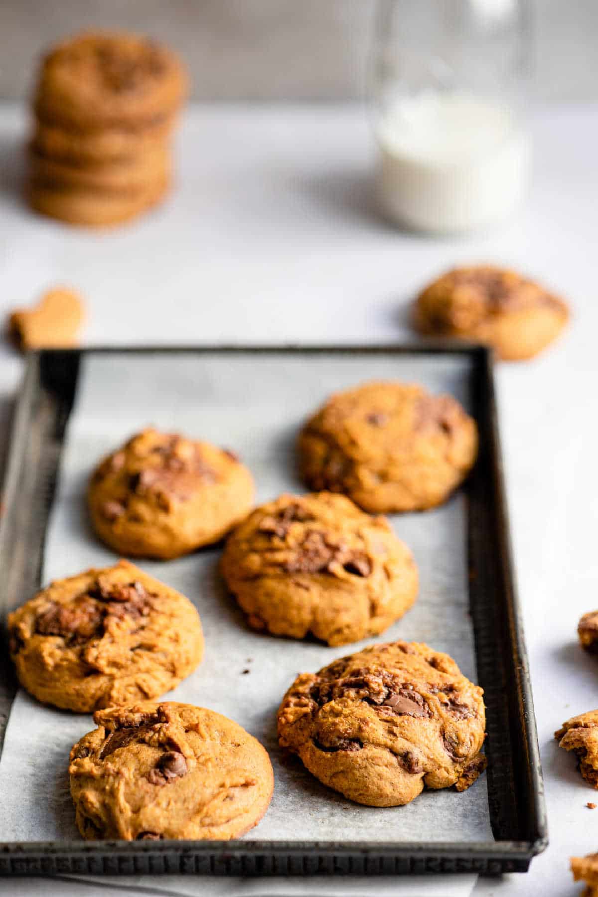 Pumpkin chocolate chip cookies on a baking sheet next to a glass of milk. 