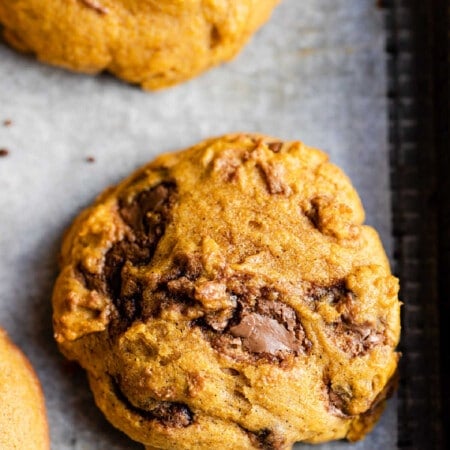 Close up photo of a pumpkin chocolate chip cookie on a baking sheet.