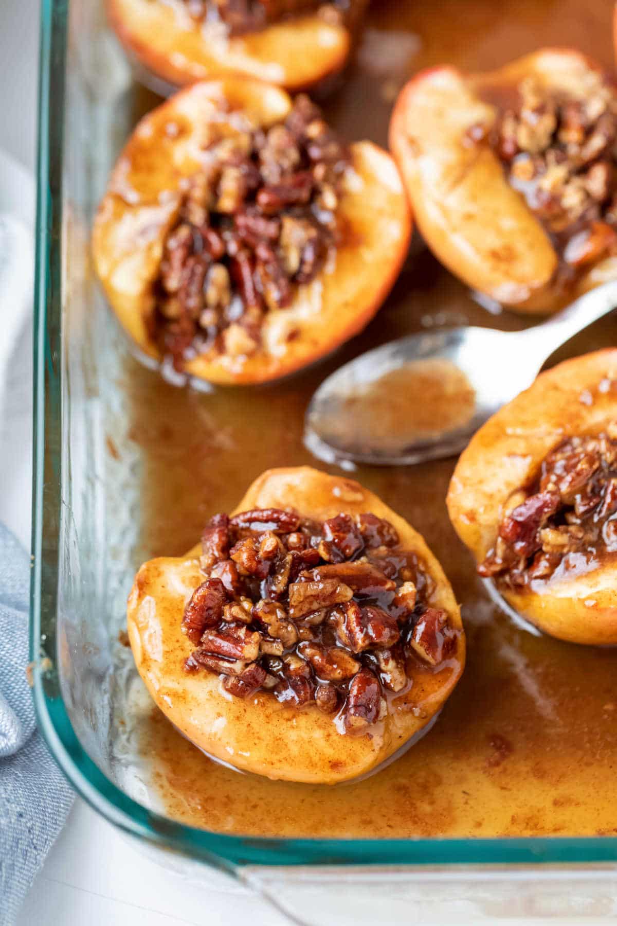 A spoon in caramel sauce next to baked apples. 