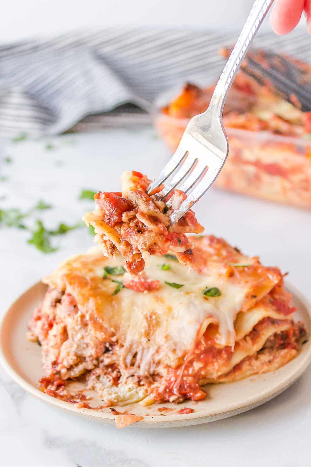 Fork taking a bite from a slice of lasagna.