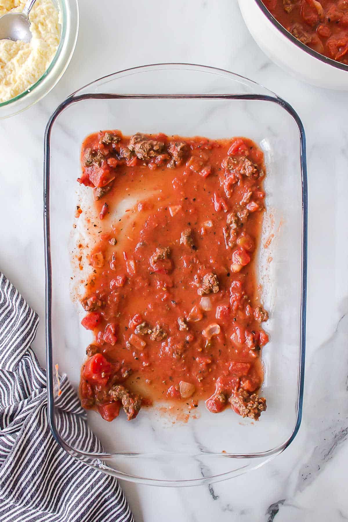 Red sauce spread in the bottom of a baking pan.