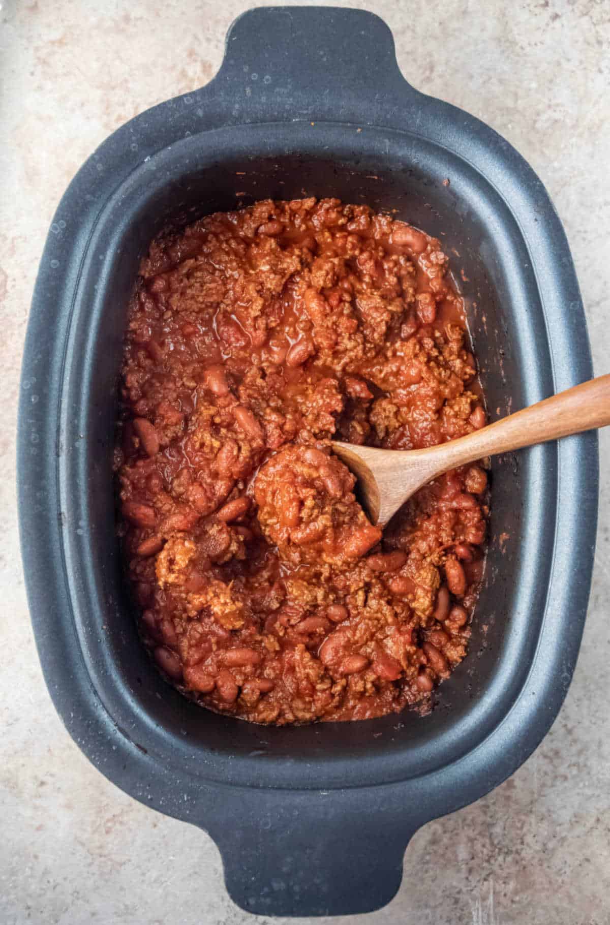 Wooden spoon in a crock pot full of chili. 