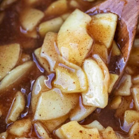 Wooden spoon stirring apple pie filling.