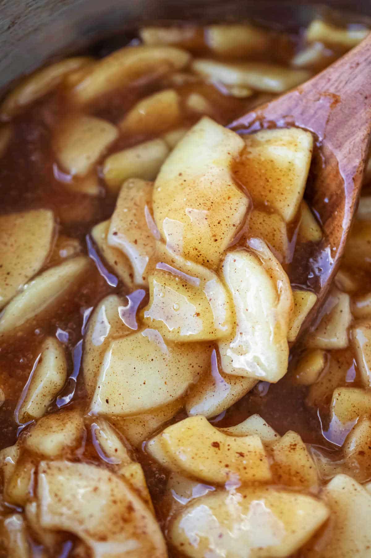Wooden spoon stirring apple pie filling.