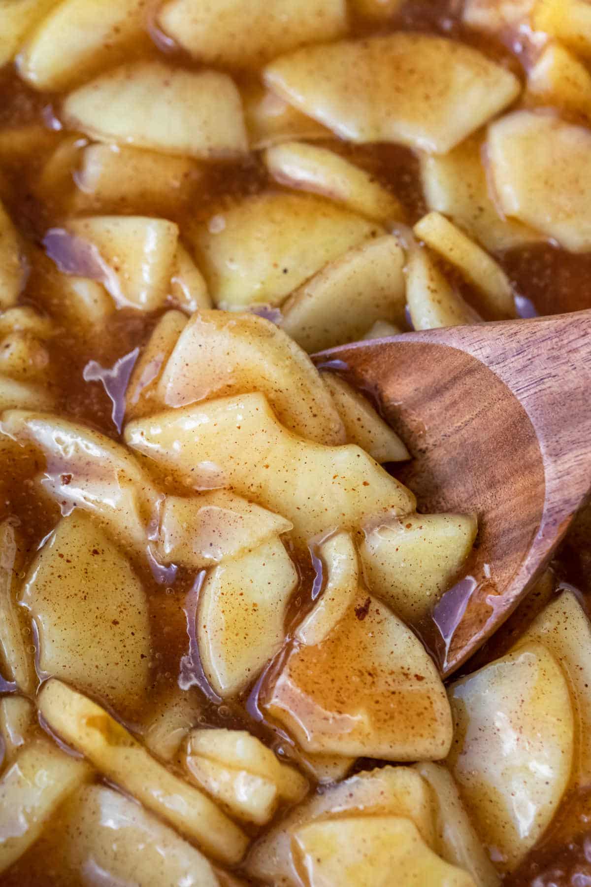 A wooden spoon scooping up apple pie filling. 