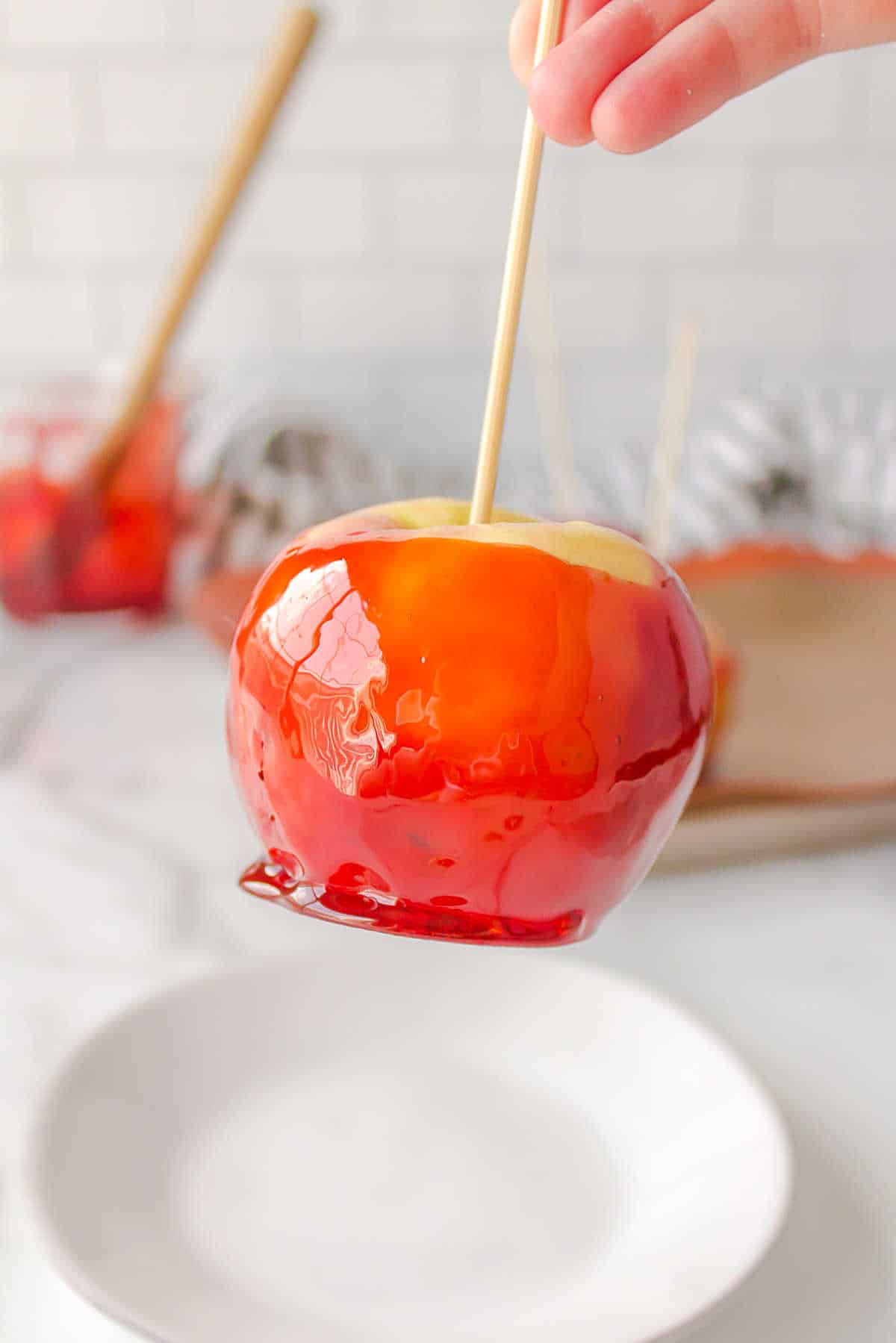 Hand lifting up a candy apple off of a white plate. 