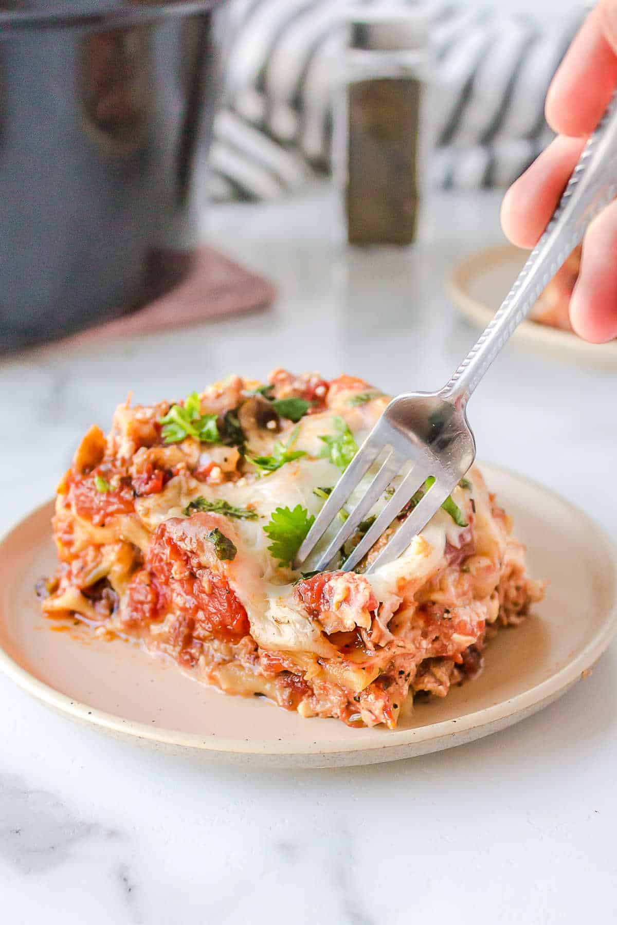 A fork taking a bite of a piece of lasagna.