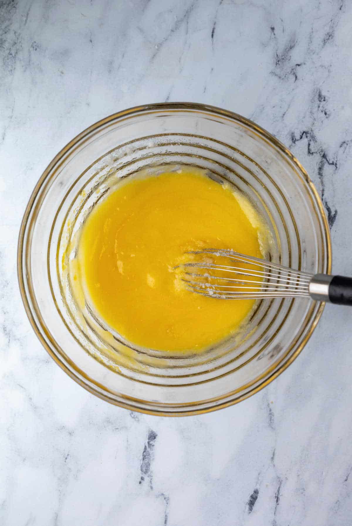 Eggs whisked into oil and sugar in a white mixing bowl.
