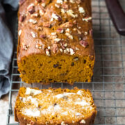 Loaf of pumpkin nut bread with one buttered slice next to it.