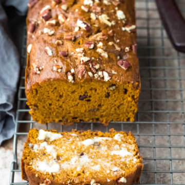 Loaf of pumpkin nut bread with one buttered slice next to it.