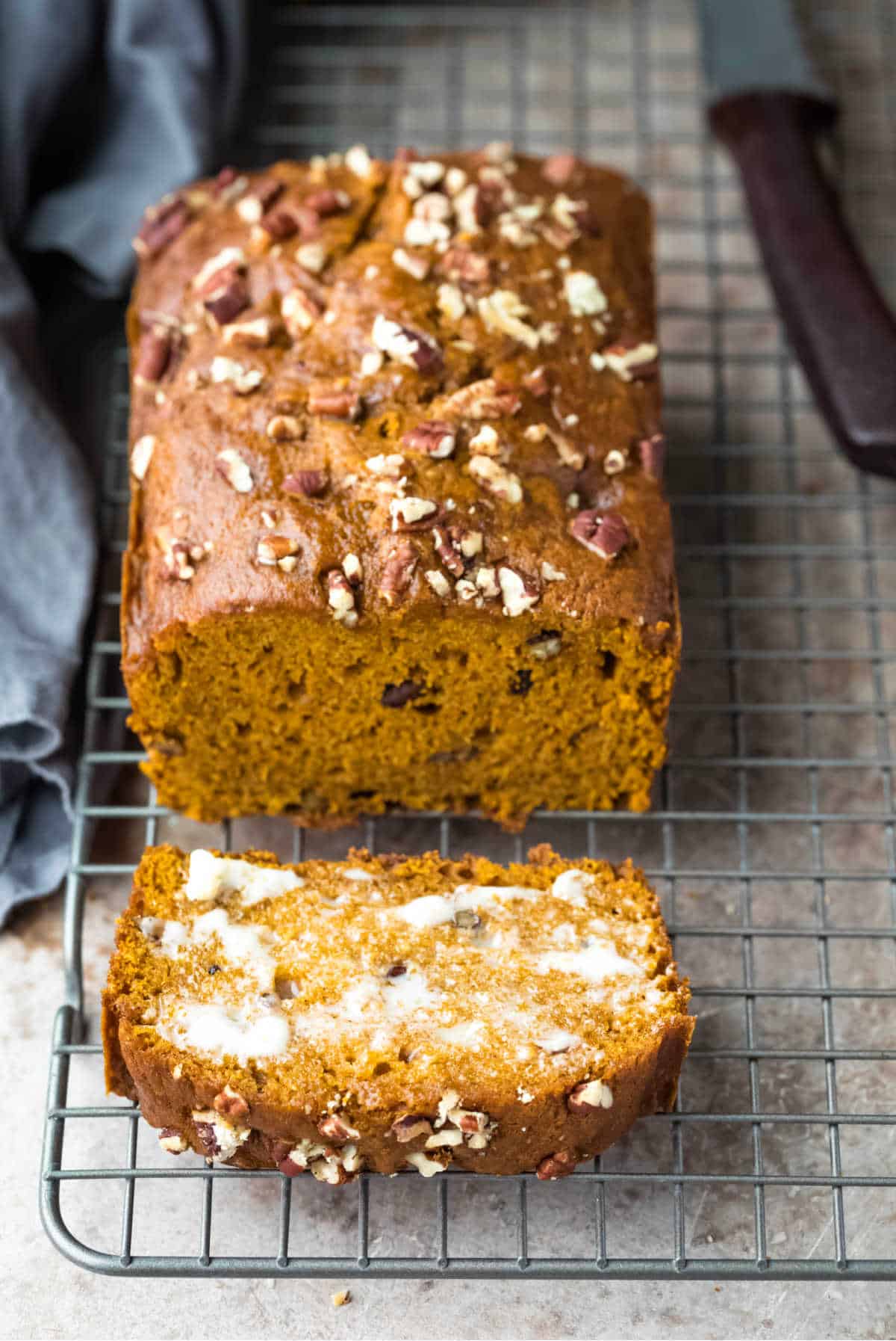 Loaf of pumpkin nut bread with one buttered slice next to it. 