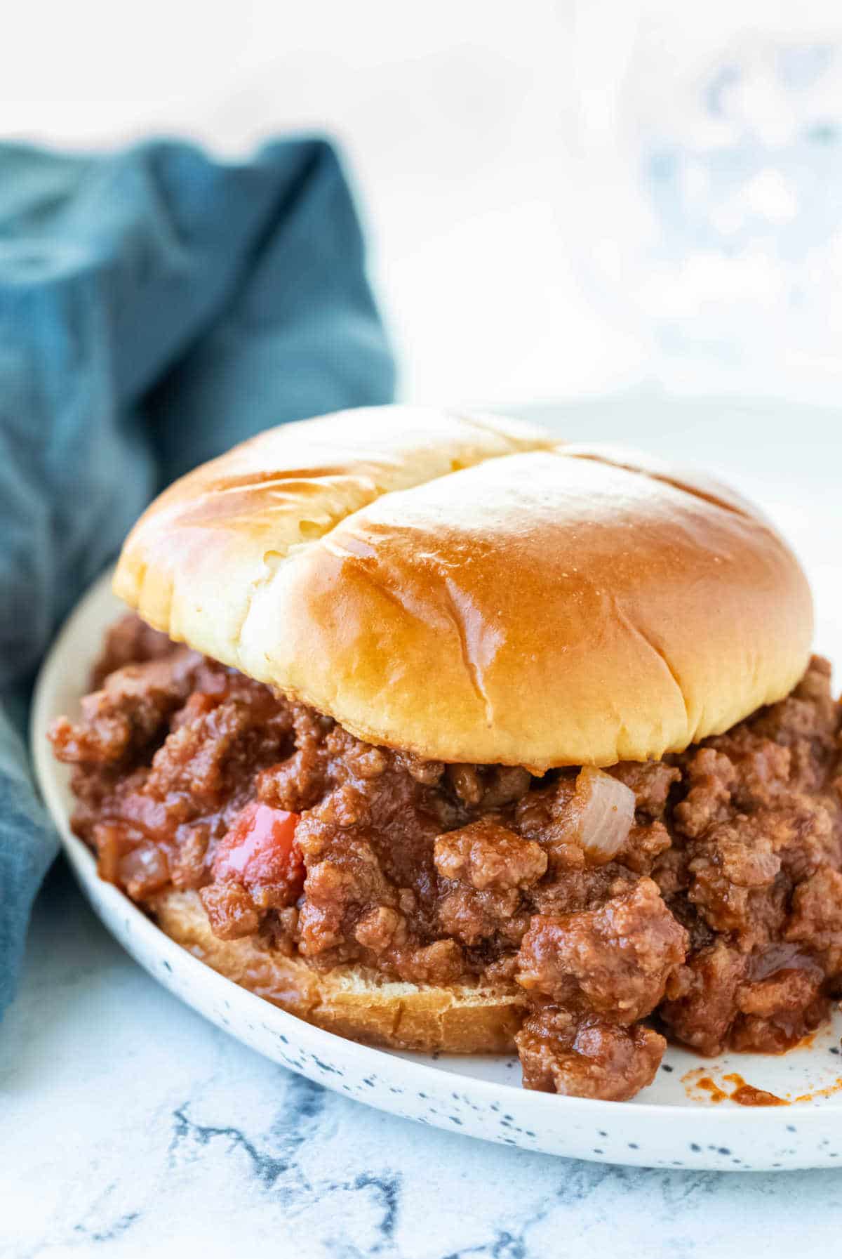 Sloppy joe on a plate next to a blue napkin. 