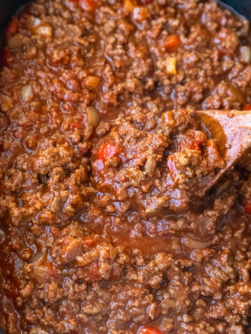 Wooden spoon stirring sloppy joes in a slow cooker.