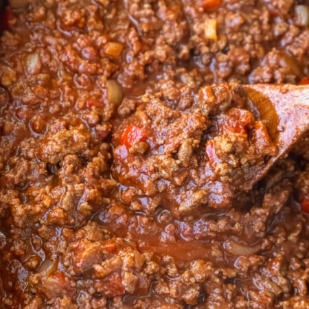 Wooden spoon stirring sloppy joes in a slow cooker.