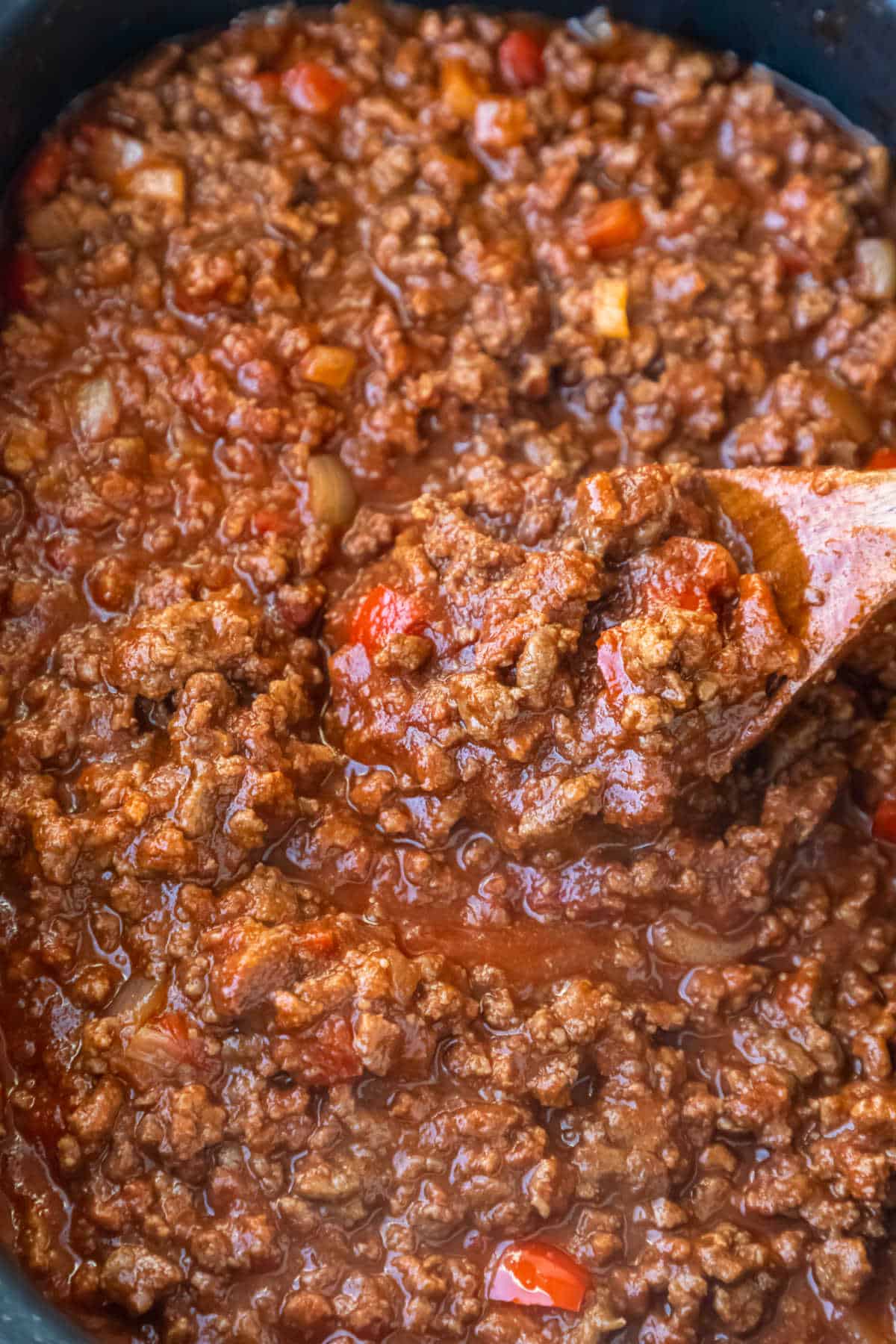 Wooden spoon stirring sloppy joes in a slow cooker.