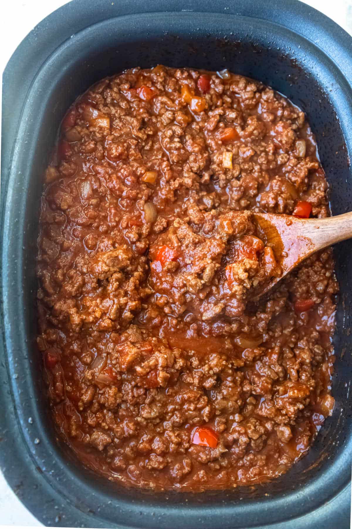 Wooden spoon scooping sloppy joe from a crock pot.