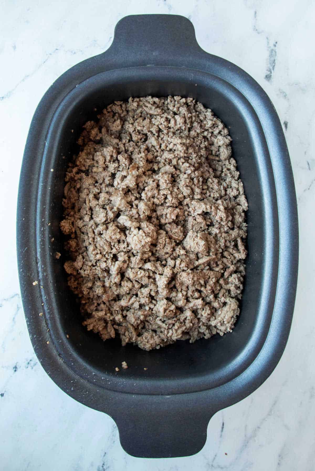 Browned ground beef in a slow cooker insert. 