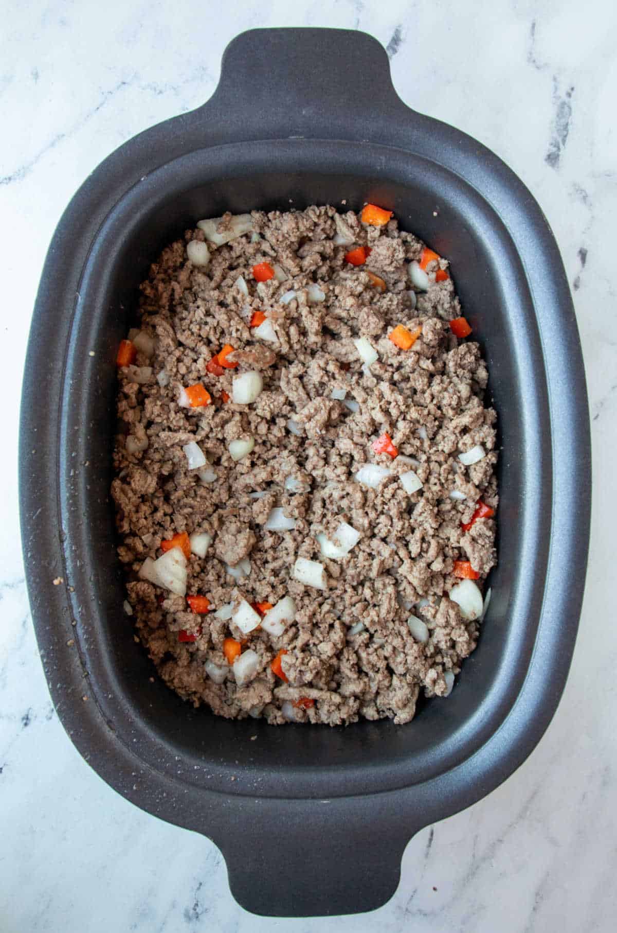 Browned ground beef onion and bell pepper in a slow cooker. 