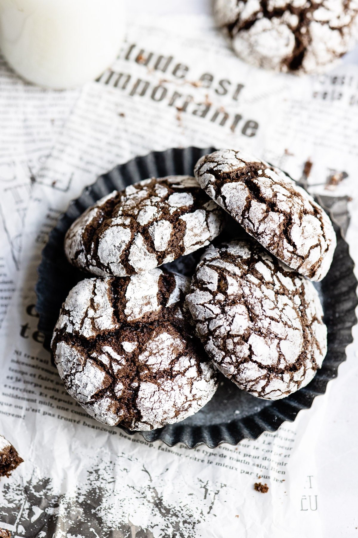 Chocolate crinkle cookies in a metal dish next to a glass of milk. 