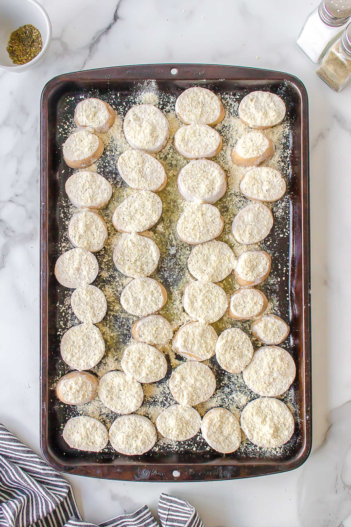 Slices of coated potato in butter in a jelly roll pan. 