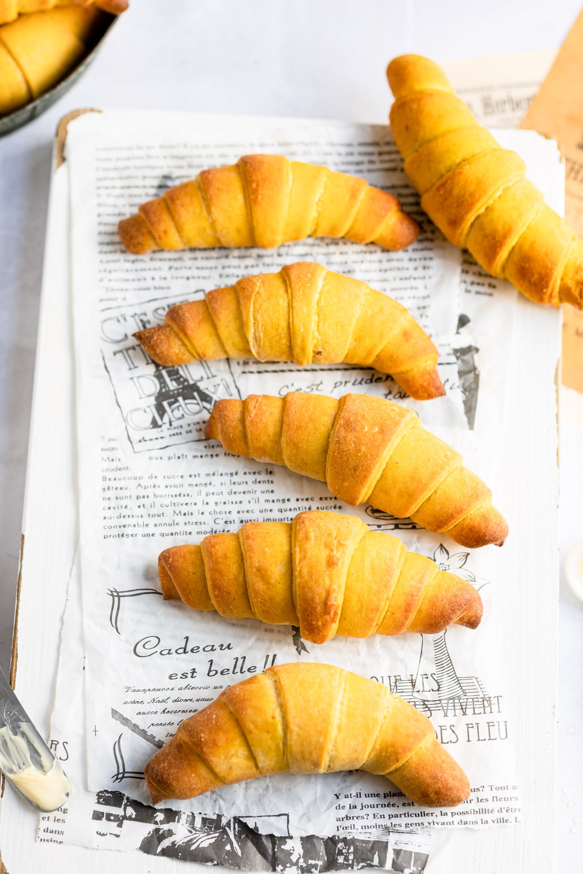 Pumpkin crescent rolls in a line on a piece of parchment paper. 