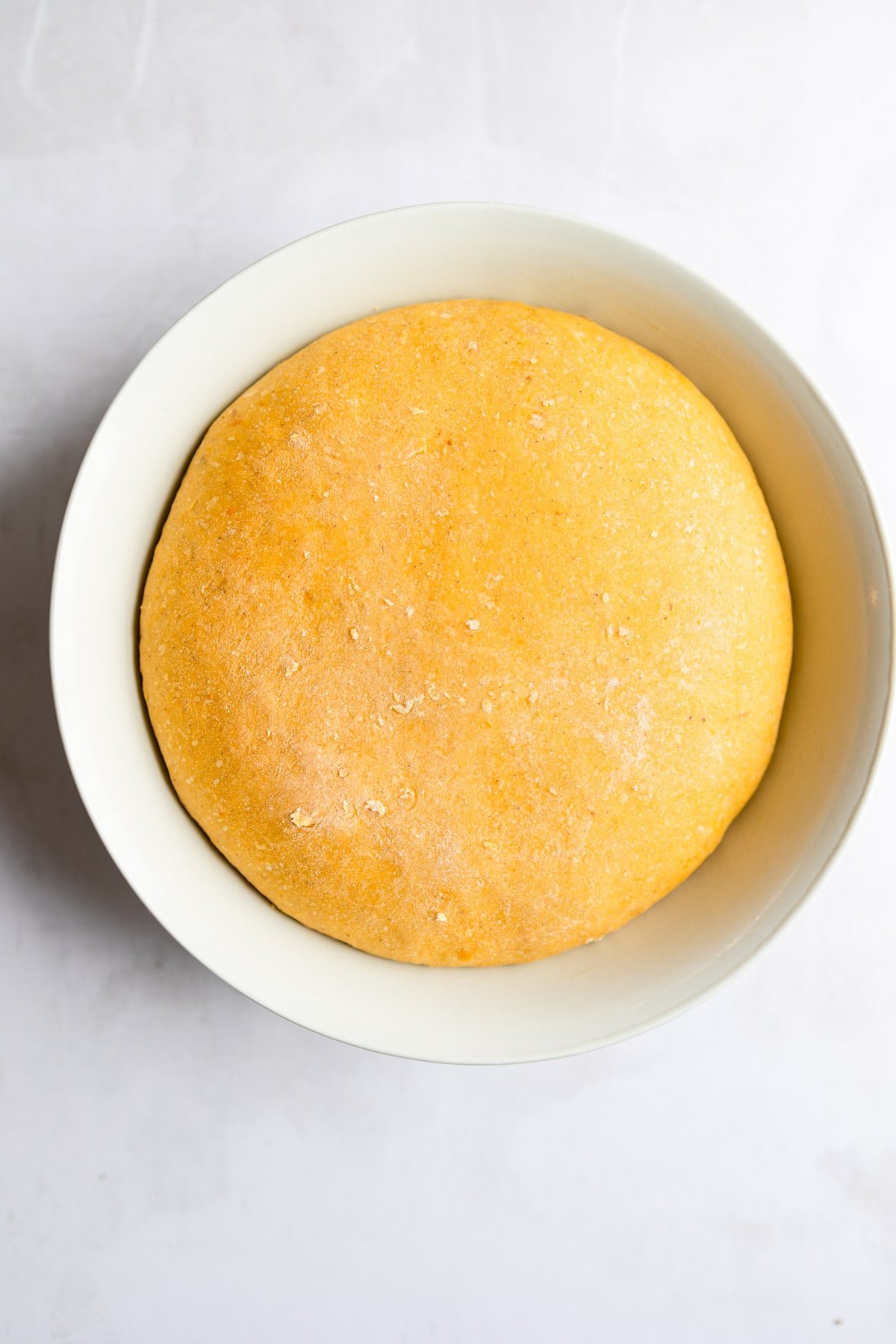 Risen pumpkin roll dough in a white bowl. .