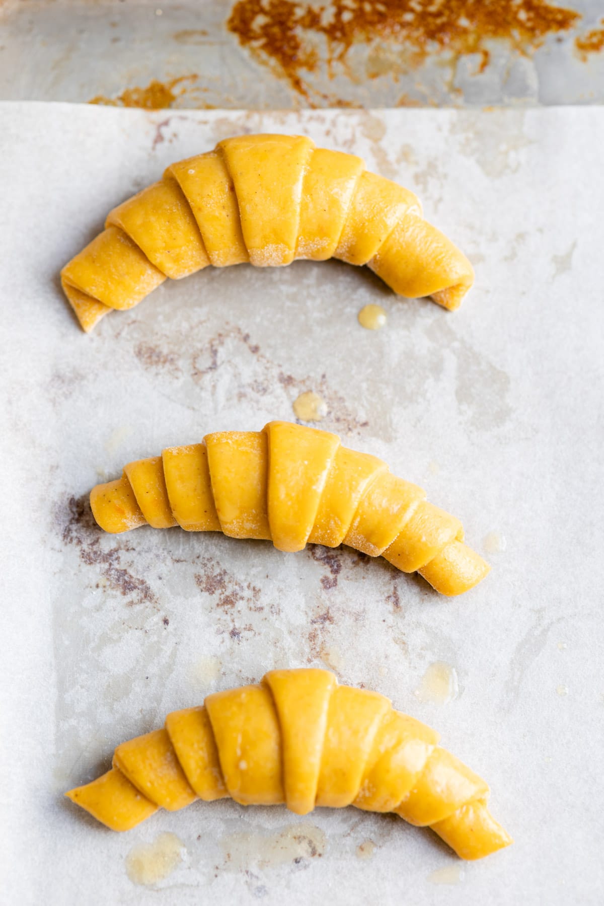 Unbaked pumpkin crescent rolls on a piece of parchment paper. 