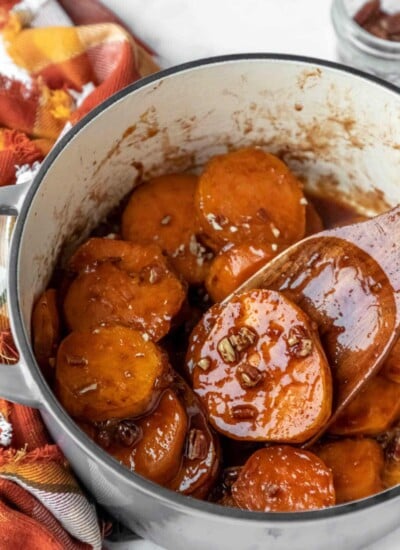 A wooden spatula scooping up a candied sweet potato from a Dutch oven.