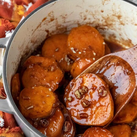 A wooden spatula scooping up a candied sweet potato from a Dutch oven.