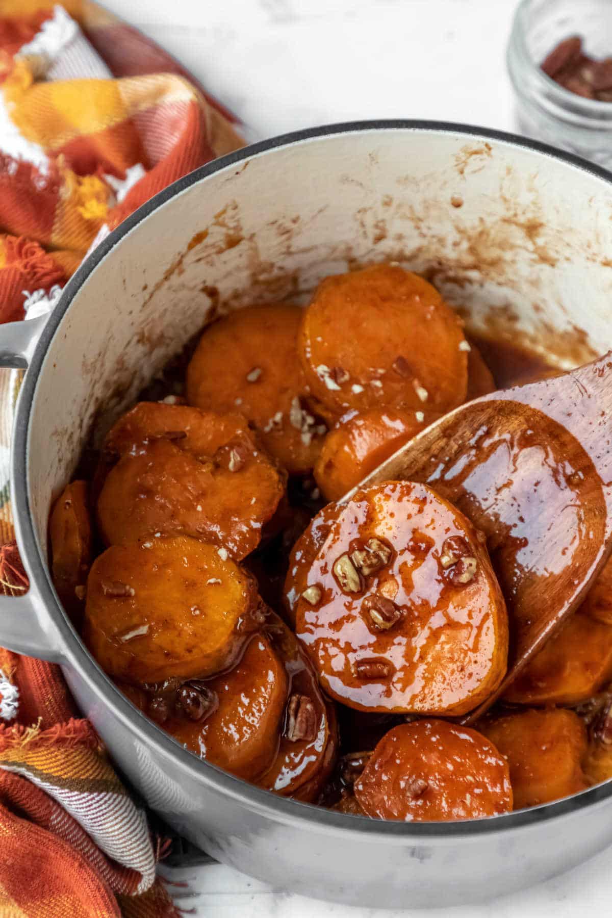 A wooden spatula scooping up a candied sweet potato from a Dutch oven.