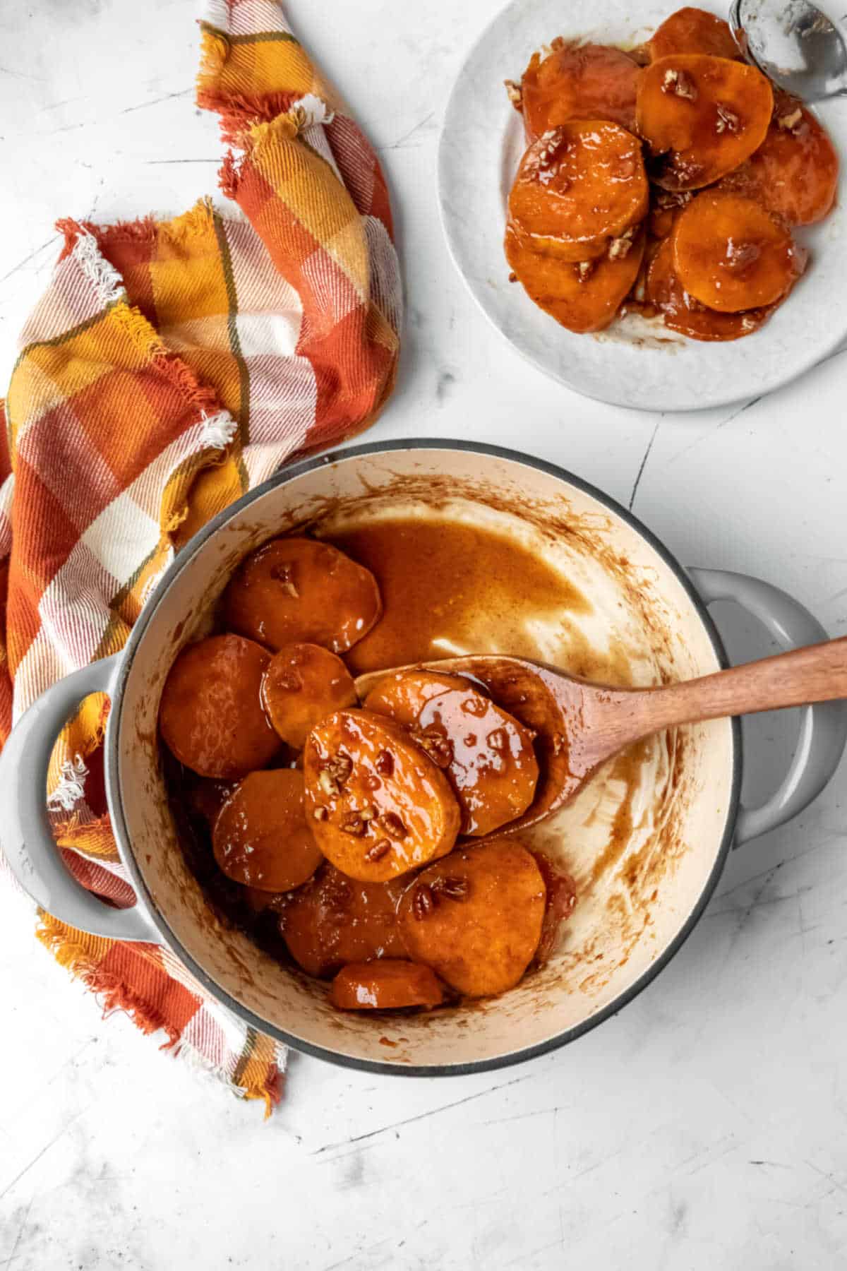 Dutch oven with candied sweet potatoes next to a plate of candied sweet potatoes.