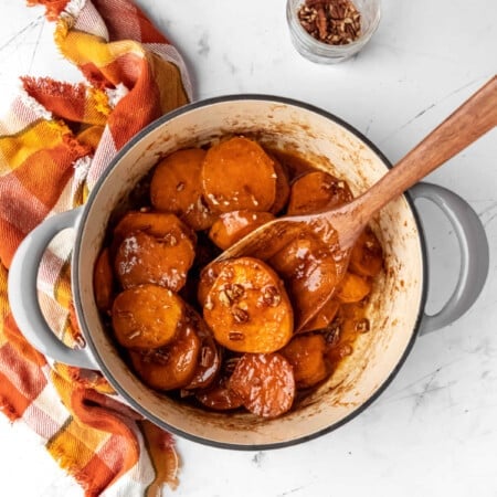 Dutch oven with candied sweet potatoes next to a dish of pecans.