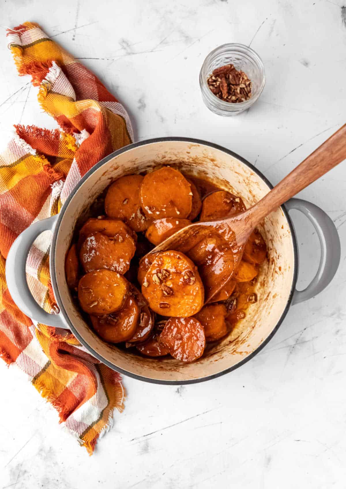 Dutch oven with candied sweet potatoes next to a dish of pecans. 
