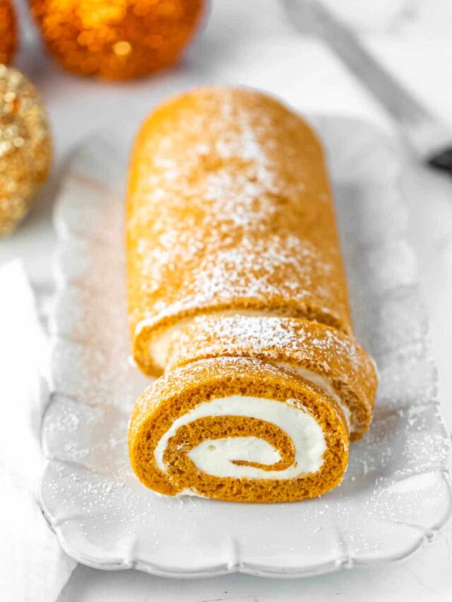Pumpkin roll with two slices cut on a white platter.