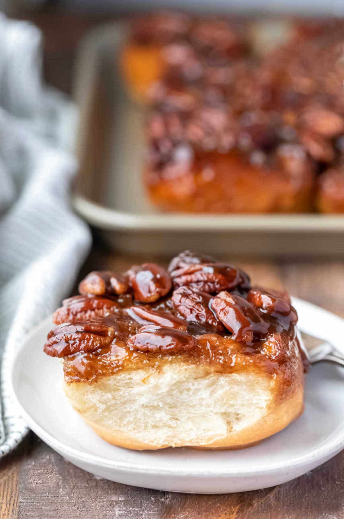 A maple sticky bun and a fork on a white plate. 