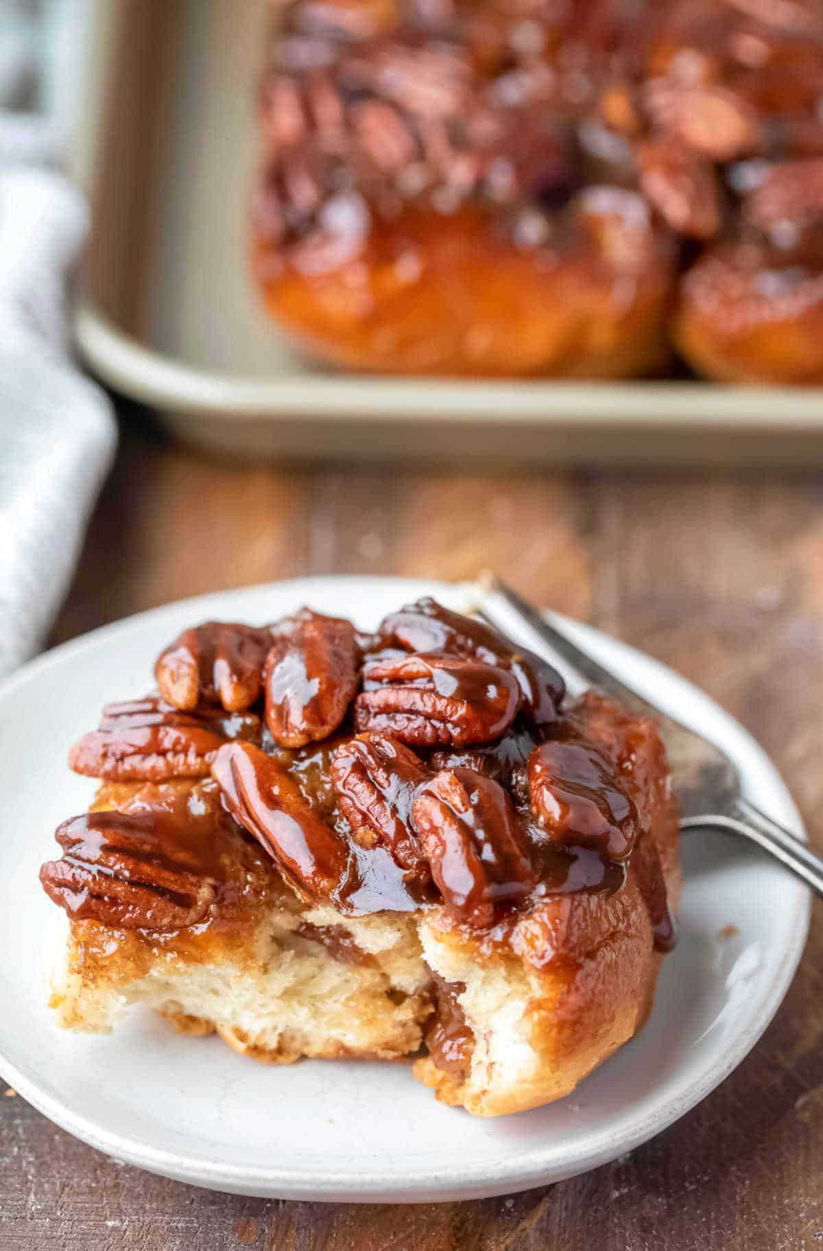 A maple sticky bun on a white plate with a bite out of it. 