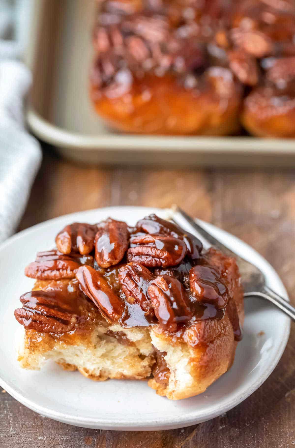 A maple sticky bun on a white plate with a bite out of it.