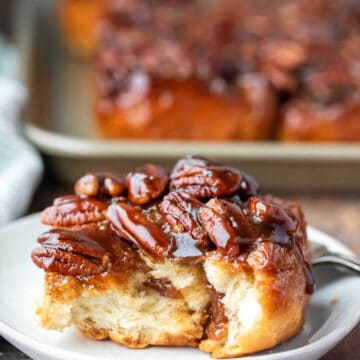 Maple sticky bun on a white plate with a piece missing from the front.